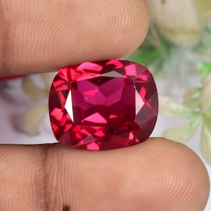 Op de afbeelding: Een dieprode edelsteen met een kussen-slijpsel. De edelsteen wordt in een hand gehouden.