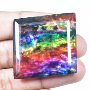 Op de afbeelding: Een grote, iriserende edelsteen met een vierkante vorm en een regenboog van kleuren, waaronder rood, oranje, geel, groen, blauw, indigo en violet.