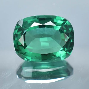 Puede incluir: Una gema verde vibrante con forma ovalada facetada. La gema está tallada y pulida para un alto brillo, mostrando su brillo y claridad.