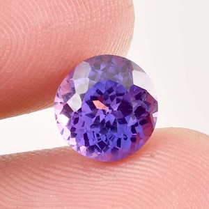 Puede incluir: Una piedra preciosa redonda y facetada de color púrpura con un patrón en forma de estrella en el centro.