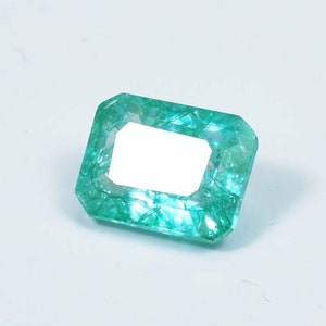 May include: A vibrant green emerald gemstone with a rectangular cut and a faceted finish.