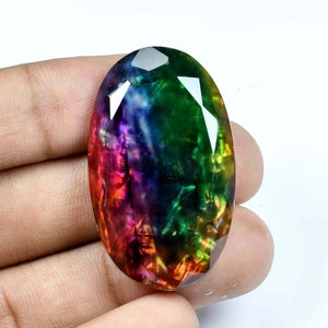 May include: A large, oval-shaped gemstone with a rainbow of colors, including red, orange, yellow, green, blue, indigo, and violet. The gemstone is cut and polished, and it has a high degree of brilliance.