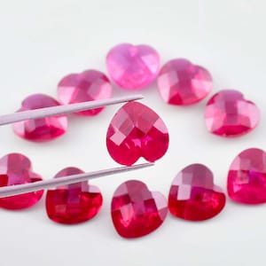 Op de afbeelding: Een verzameling van tien hartvormige edelstenen in verschillende tinten roze en rood. De edelstenen zijn gefacetteerd en hebben een hoge glans.