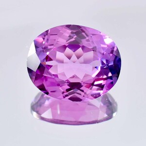 May include: A vibrant purple oval-shaped gemstone with a faceted cut. The gemstone is reflecting light, showcasing its brilliance.