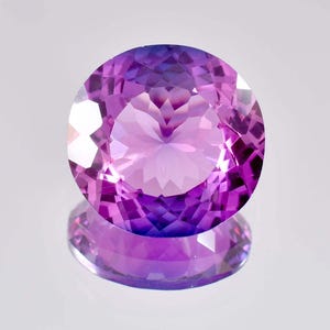 Puede incluir: Una gran gema de amatista de forma ovalada con un degradado de color púrpura y rosa. La gema está facetada y tiene un alto pulido.