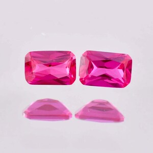 May include: Two vibrant pink rectangular gemstones with a faceted cut. The gemstones are set against a white background.