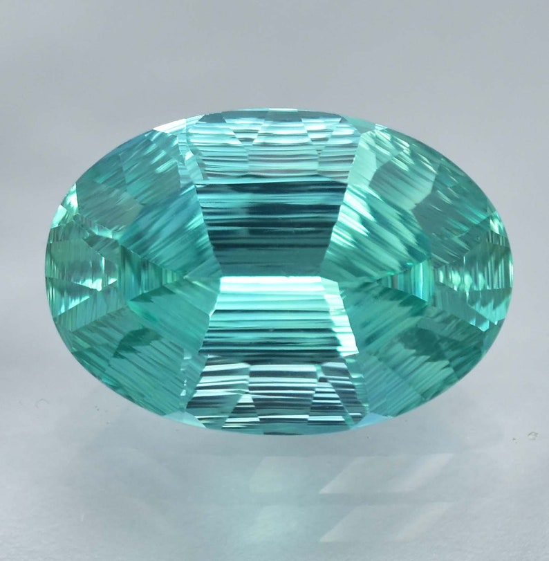 May include: A vibrant teal green gemstone with a faceted oval shape. The gem has a unique striated pattern, creating a mesmerizing visual effect.