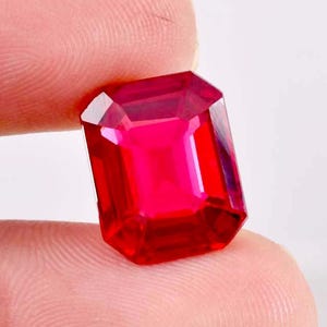 Puede incluir: Una gema roja vibrante con un corte esmeralda rectangular.