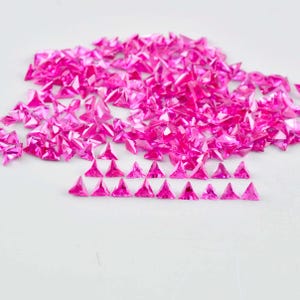Puede incluir: Un montón grande de piedras preciosas triangulares rosas, con una fila de piedras preciosas triangulares rosas más pequeñas en frente.