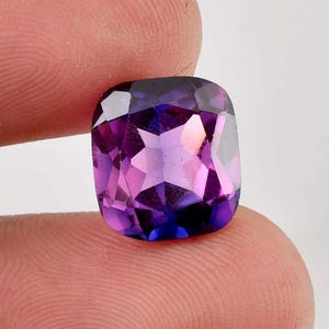 Puede incluir: Una gran gema de talla cojín con un tono púrpura profundo. La gema tiene un ligero tono azul y está facetada con un patrón de estrella.