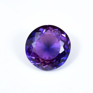 May include: A round, faceted gemstone with a purple to blue gradient. The gemstone is cut in a round brilliant shape and has a high degree of brilliance.
