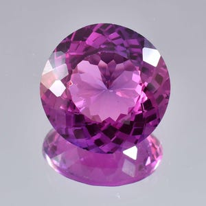 Puede incluir: Una piedra preciosa redonda y facetada con un tono púrpura. La piedra preciosa está tallada para crear un patrón de estrella en el centro.