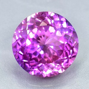 May include: A vibrant purple gemstone with a faceted cut. The gem has a round shape and a high degree of brilliance.