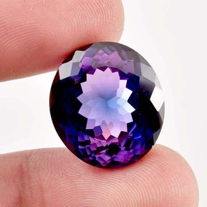 以下が含まれることがあります： 紫から青へのグラデーションカラーの、大きな楕円形のファセットカットされたアメジストの宝石。宝石は星形の模様でカットされています。