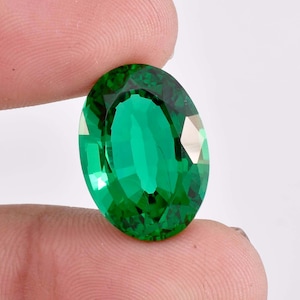 Puede incluir: Una gema ovalada de color verde vibrante con un corte facetado. La gema se sostiene en una mano, mostrando su brillo y claridad.