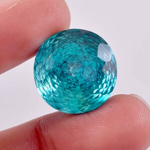 May include: A large, round, teal blue gemstone with a faceted cut. The gemstone has a shimmering, iridescent quality.