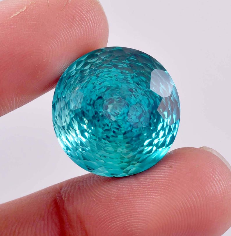 May include: A large, round, teal blue gemstone with a faceted cut. The gemstone has a shimmering, iridescent quality.