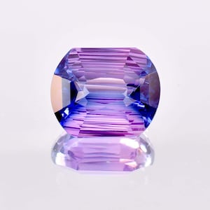 May include: A faceted gemstone with a purple and blue color gradient. The gemstone is cut in an oval shape and has a high polish.