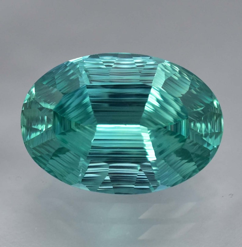 May include: A vibrant teal green oval-shaped gemstone with a faceted cut. The gemstone has a smooth, polished surface and a clear, transparent appearance.