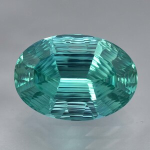 May include: A vibrant teal blue gemstone with a faceted oval cut. The gemstone has a striated pattern and a high polish.