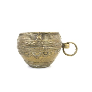 May include: A vintage brass cup with intricate etched patterns and a small handle. The cup has a rounded body and a decorative rim. The handle is a simple ring shape. The cup is likely used for decorative purposes.