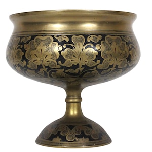May include: A gold metal bowl with a black and gold floral design. The bowl is on a pedestal with a matching design.