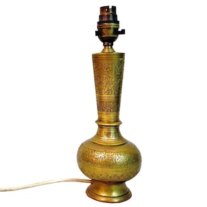 Pode incluir: Uma luminária de mesa de latão vintage com um design floral gravado e ornamentado. A luminária tem um soquete de lâmpada na parte superior e uma base decorativa. A luminária tem aproximadamente 38 cm de altura e possui um cabo de alimentação.