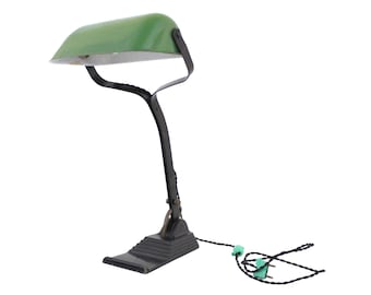 Könnte beinhalten: Eine vintage Schreibtischlampe aus grünem Glas mit einem verstellbaren Arm und Sockel aus schwarzem Metall. Die Lampe hat ein Kabel mit einem zweipoligen Stecker.