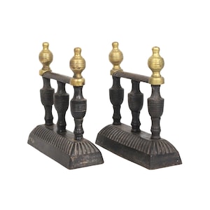 May include: A pair of fireplace andirons featuring dark cast iron bases with ribbed detailing. Each andiron has three vertical supports, with the two outer supports topped by polished brass finials in a spherical, ribbed shape.