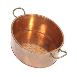 Könnte beinhalten: Ein ovales Kupferbecken mit polierter metallischer Oberfläche und zwei geschwungenen Messinggriffen, die seitlich mit Nieten befestigt sind. Das Innere weist Anzeichen von natürlicher Oxidation und Abnutzung auf, mit einem glatten Rand.