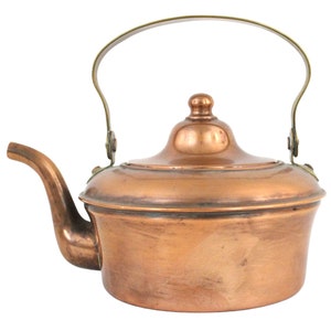 May include: A copper kettle with a brass handle and lid. The kettle has a rounded body and a spout on the side.