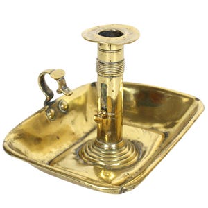 Può includere: Un candelabro in ottone con una base rettangolare e uno spegnicandela rimovibile. Il candelabro ha una colonna decorata a canne e un manico ad anello.