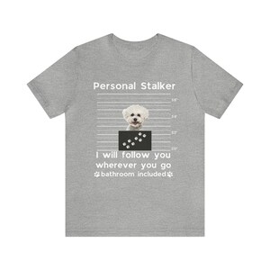 May include: A gray t-shirt with a white graphic of a white dog with black paw prints. The text "Personal Stalker" is above the dog and the text "I will follow you wherever you go bathroom included" is below the dog.