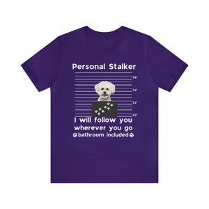 May include: Purple t-shirt with a white graphic of a white dog in a mugshot with the text "Personal Stalker" and "I will follow you wherever you go bathroom included".