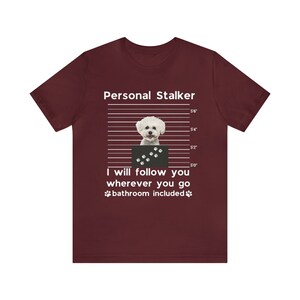May include: A maroon t-shirt with a white graphic of a small white dog in a mugshot. The text "Personal Stalker" is above the dog and "I will follow you wherever you go bathroom included" is below the dog.
