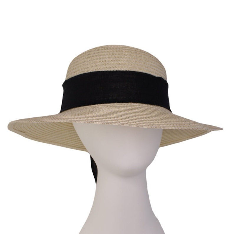 Pu&ograve; includere: Un cappello di paglia a tesa larga con un nastro nero legato attorno alla corona. Il nastro ha una lunga coda che pende dalla parte posteriore del cappello.