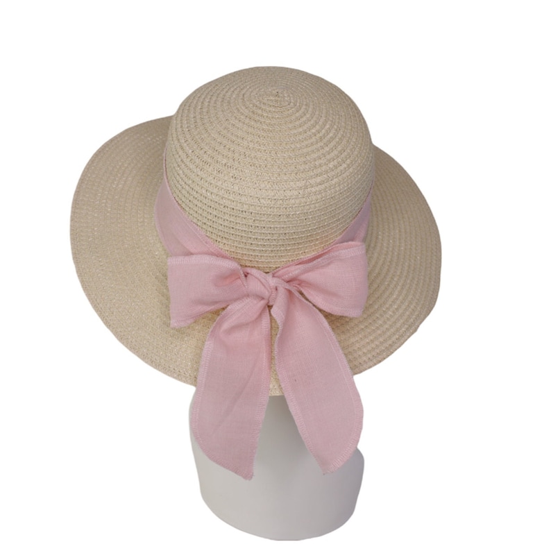 Pu&ograve; includere: Un cappello di paglia a tesa larga con un nastro rosa legato in un fiocco. Il cappello &egrave; beige e ha una trama intrecciata.