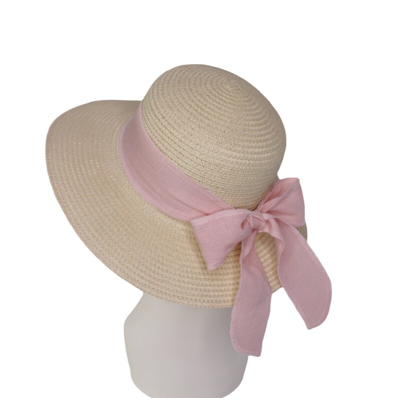 Pu&ograve; includere: Un cappello di paglia da sole con un'ampia tesa e un nastro rosa legato in un fiocco sul retro.