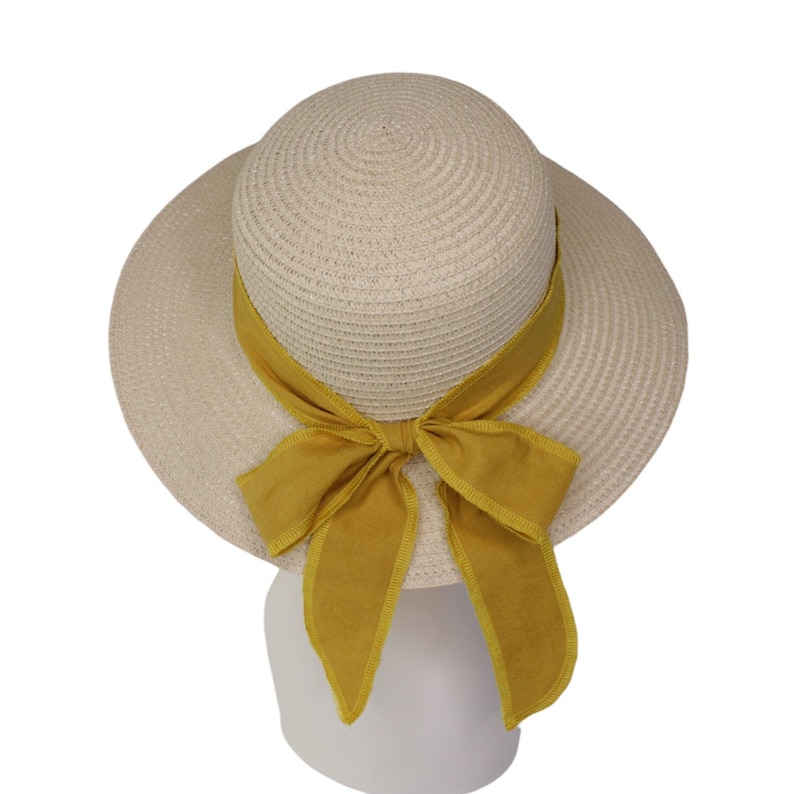 Pu&ograve; includere: Un cappello di paglia beige con un'ampia tesa e un fiocco di stoffa giallo.