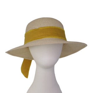 Pu&ograve; includere: Un cappello di paglia a tesa larga con un nastro giallo legato attorno alla corona. Il nastro &egrave; legato in un fiocco sul retro del cappello.