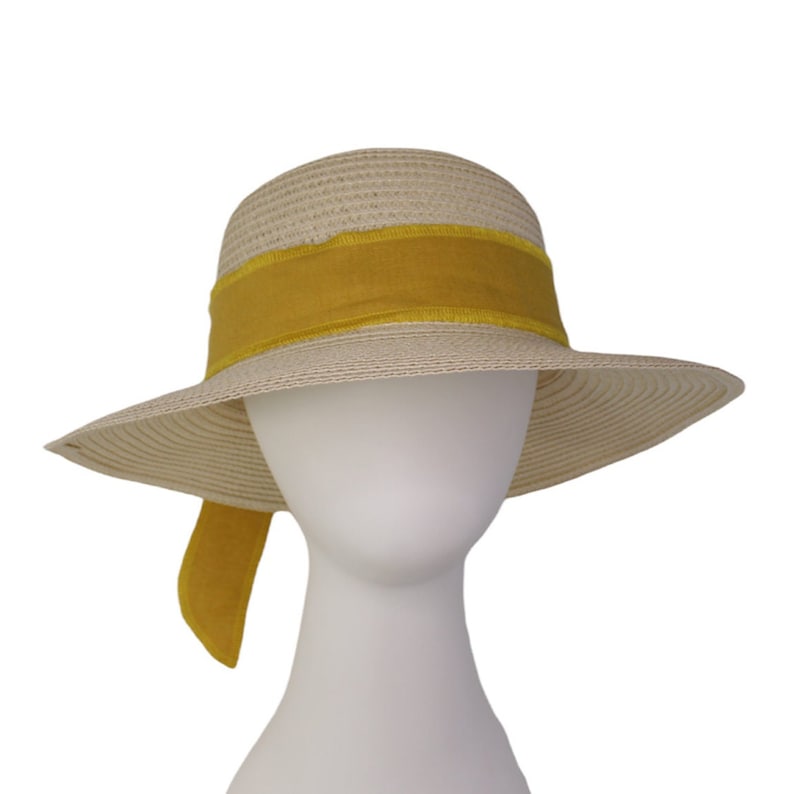 Pu&ograve; includere: Un cappello di paglia a tesa larga con un nastro giallo legato attorno alla corona. Il nastro &egrave; legato in un fiocco sul retro del cappello.