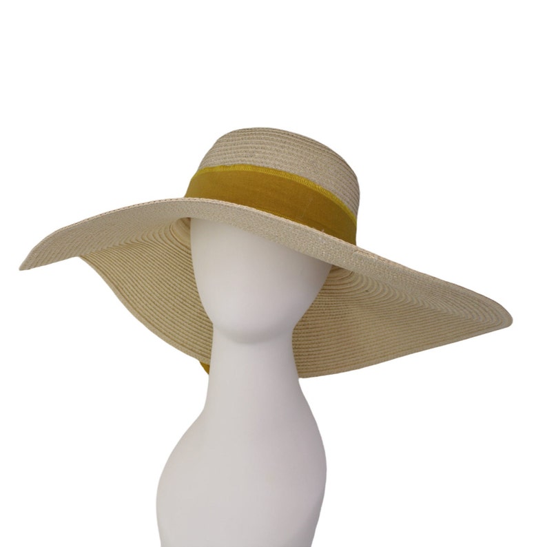 Pu&ograve; includere: Un cappello di paglia a tesa larga con un nastro giallo. Il cappello &egrave; beige e ha una tesa larga e morbida.