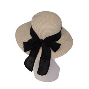 Pu&ograve; includere: Un cappello di paglia beige con un'ampia tesa e un fiocco di tessuto nero legato sul davanti.