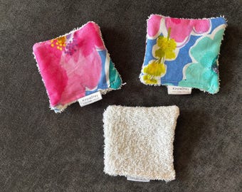 May include: Three square reusable face cloths. Two cloths feature a floral pattern in pink, blue, and green. The third cloth is white. Each cloth has a small tag that reads "KinzieShay".