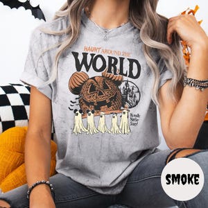 May include: Gray t-shirt with a Halloween-themed graphic. The design features a Mickey Mouse-shaped jack-o'-lantern, ghosts, and the text "Haunt Around the World." The shirt also has the text "It's really Not-So-Scary!"