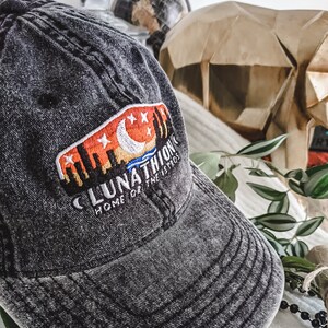 May include: A black denim baseball cap with a white embroidered patch that says "Lunathion Home of the Astros" with a crescent moon and stars in the background.