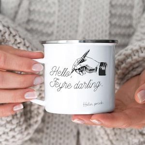 May include: White enamel mug with a black and white illustration of a hand writing "Hello, Feyre darling." The mug has a silver rim.