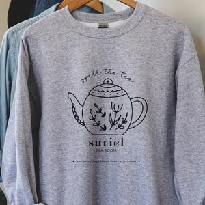 May include: Gray sweatshirt with a black and white illustration of a teapot with the text "Smell the tea" and "suriel tearoom" printed on the front.