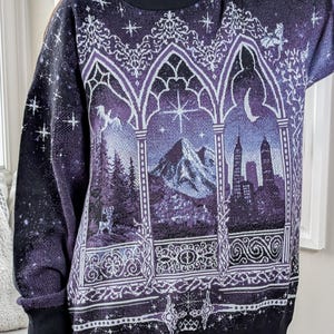 May include: A dark purple jumper with a celestial and landscape design. The jumper features a black crew neck and cuffs. The design includes mountains, a cityscape, stars, and decorative archways in white and purple.
