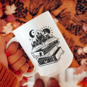 Puede incluir: Taza de cerámica blanca con una ilustración en blanco y negro de una pila de libros, un castillo y una luna creciente. El texto en la taza dice "He vivido mil vidas".